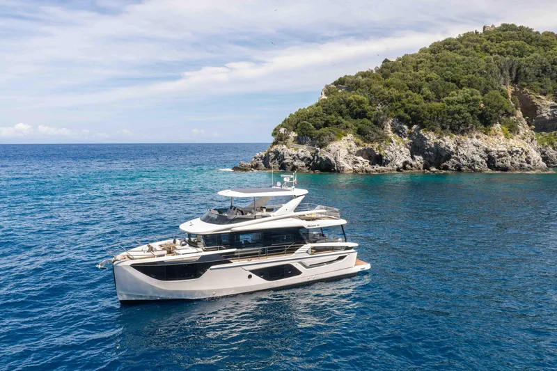 Slide: The Image of Luxurious 2026 Absolute Navetta 58 yacht cruising near a scenic rocky coastline. - 1
