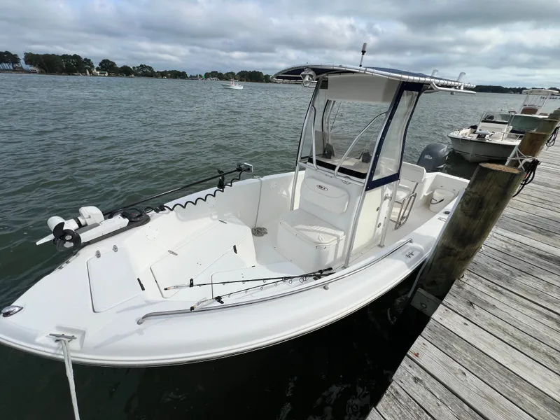 The Image of A white boat docked at a wooden pier, featuring a covered helm and fishing rods. - 0
