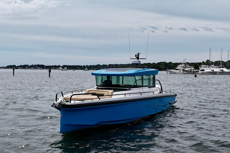 Slide: The Image of 2021 Axopar 37 XC Cross Cabin boat on calm water, with a scenic marina backdrop. - 3
