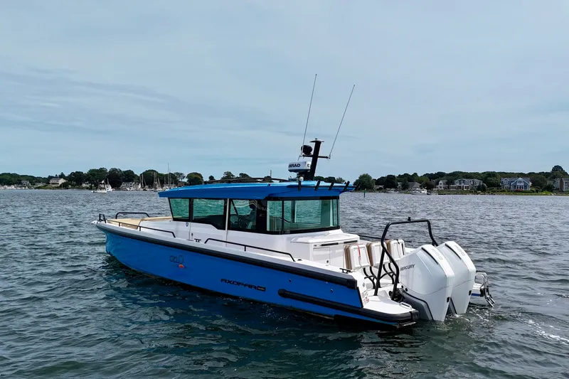 Slide: The Image of 2021 Axopar 37 XC Cross Cabin boat on calm water, near coastal homes. - 2