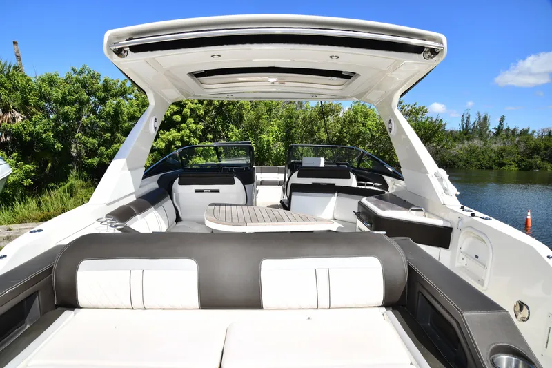 Slide: The Image of 2017 Sea Ray SLX 310 boat interior with seating and table, near lush greenery. - 36