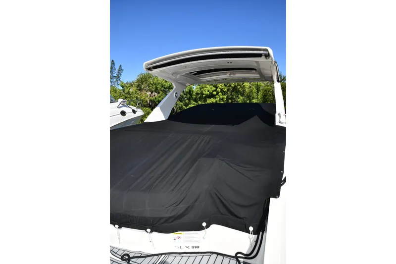 Slide: The Image of 2017 Sea Ray SLX 310 boat with black cover, sunny day, lush greenery background. - 20