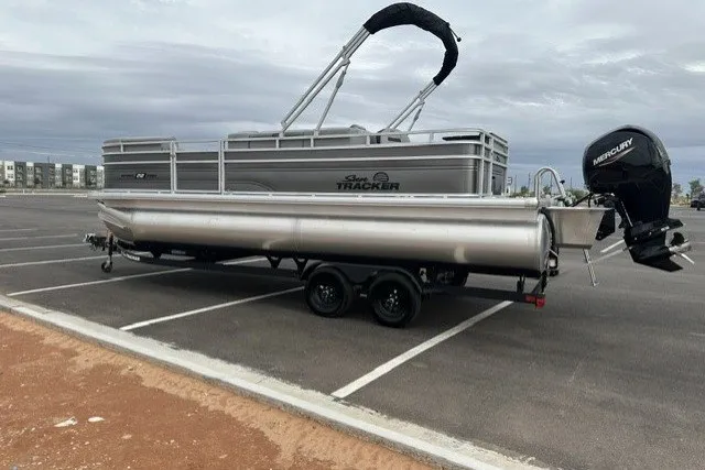 The Image of 2027 Sun Tracker SportFish 22 DLX pontoon boat on trailer in parking lot. - 0