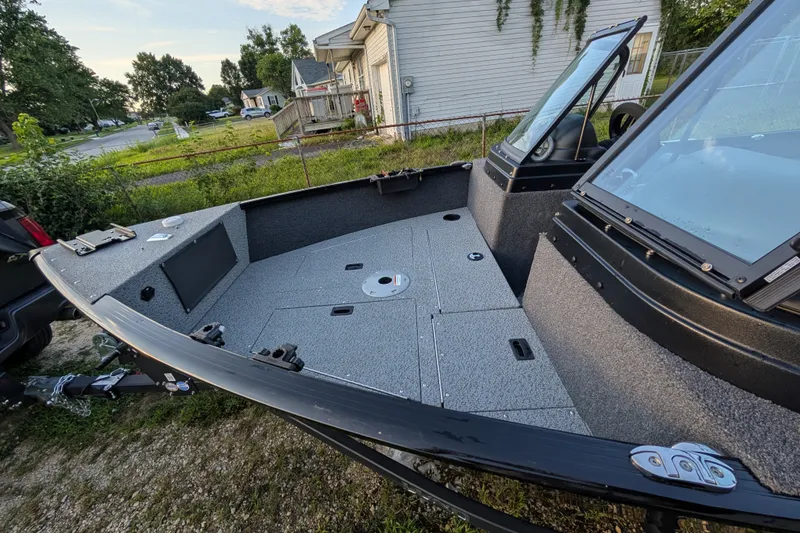 Slide: The Image of 2023 Lund 1650 Rebel XL Sport boat with spacious deck and windshield, parked outdoors. - 13