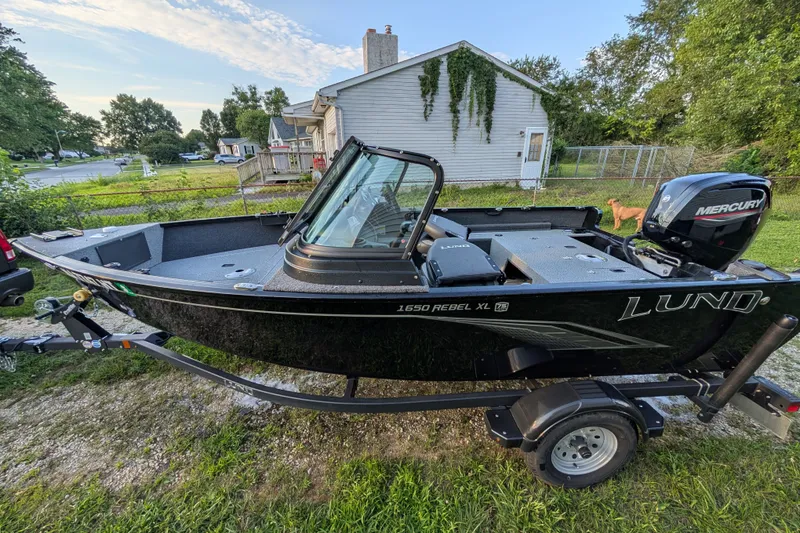 Slide: The Image of 2023 Lund 1650 Rebel XL Sport boat on trailer, parked in a residential yard. - 12