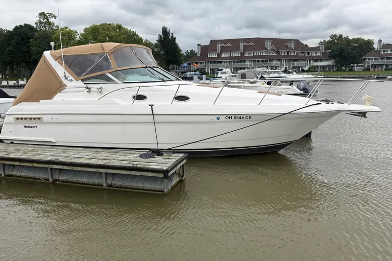 Slide: The Image of 1998 Wellcraft 3200 Martinique boat docked on a calm lake with overcast skies. - 1