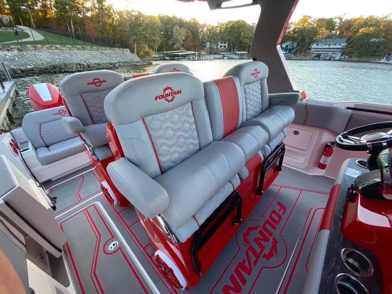 Slide: The Image of 2024 Fountain 38 SCX boat interior with red and gray seating, on a scenic lake. - 18