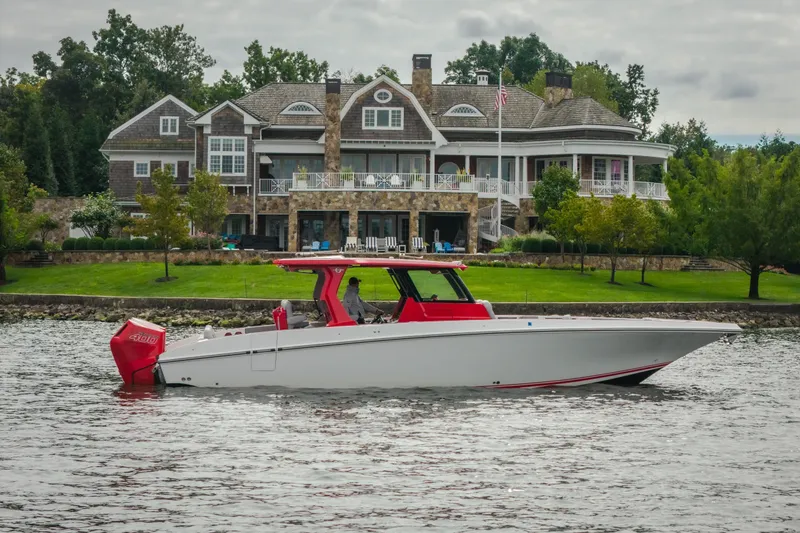 The Image of 2024 Fountain 38 SCX boat cruising near a luxurious waterfront home. - 0
