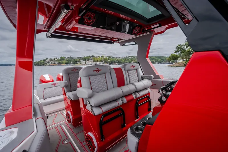 Slide: The Image of 2024 Fountain 38 SCX boat interior with red and gray seating, on a scenic lake. - 54