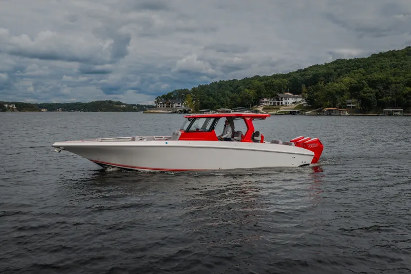 Slide: The Image of 2024 Fountain 38 SCX boat cruising on a scenic lake with lush green shoreline. - 1