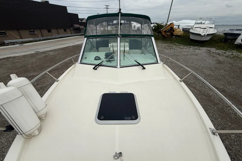 Slide: The Image of 1999 Pursuit 2460 Denali boat with windshield and deck view, parked on gravel near water. - 34