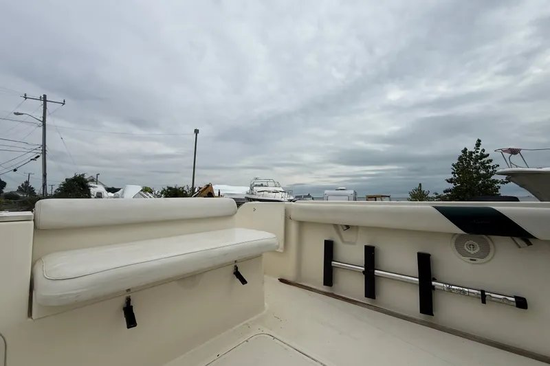 Slide: The Image of 1999 Pursuit 2460 Denali boat interior with white seating and rod holders under cloudy sky. - 19