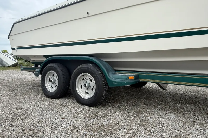 Slide: The Image of 1999 Pursuit 2460 Denali boat on a dual-axle trailer, parked on gravel. - 3