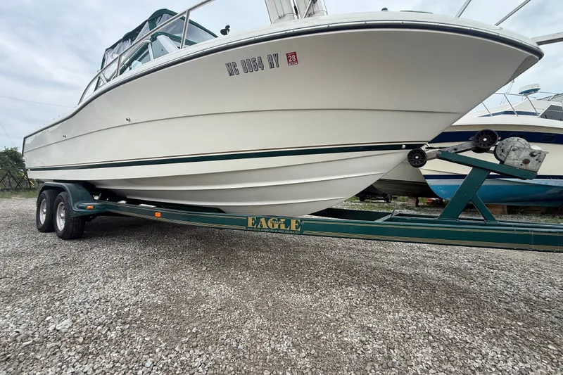 Slide: The Image of 1999 Pursuit 2460 Denali boat on a trailer, parked on gravel. - 2