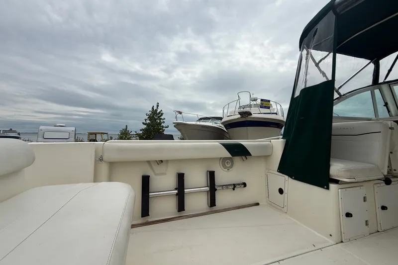 Slide: The Image of 1999 Pursuit 2460 Denali boat interior with seating and storage, under cloudy sky. - 18