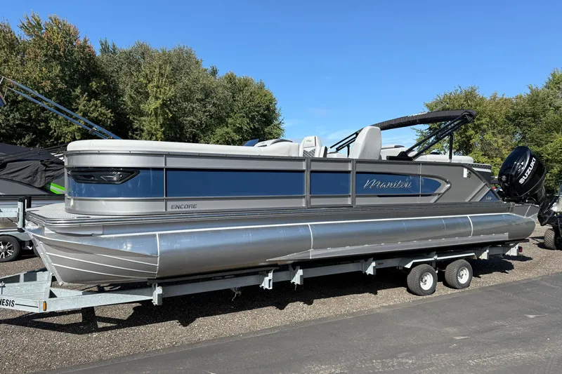 Slide: The Image of 2027 Manitou Encore 25 RF Dual pontoon boat on trailer, parked outdoors. - 2