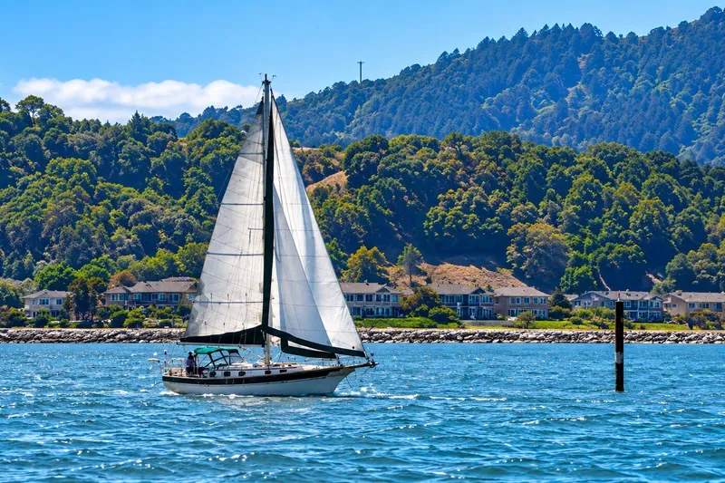 Slide: The Image of Sailboat Gozzard Cutter 36 (1988) cruising near scenic coastal homes and lush hills. - 2