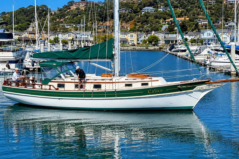 Slide: The Image of Sailboat "Calico," a 1988 Gozzard Cutter 36, docked in a scenic marina. - 5