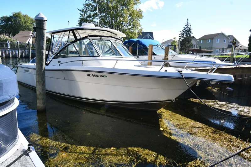 The Image of 2004 Pursuit 2670 Denali LS boat docked in a marina, surrounded by calm water. - 0