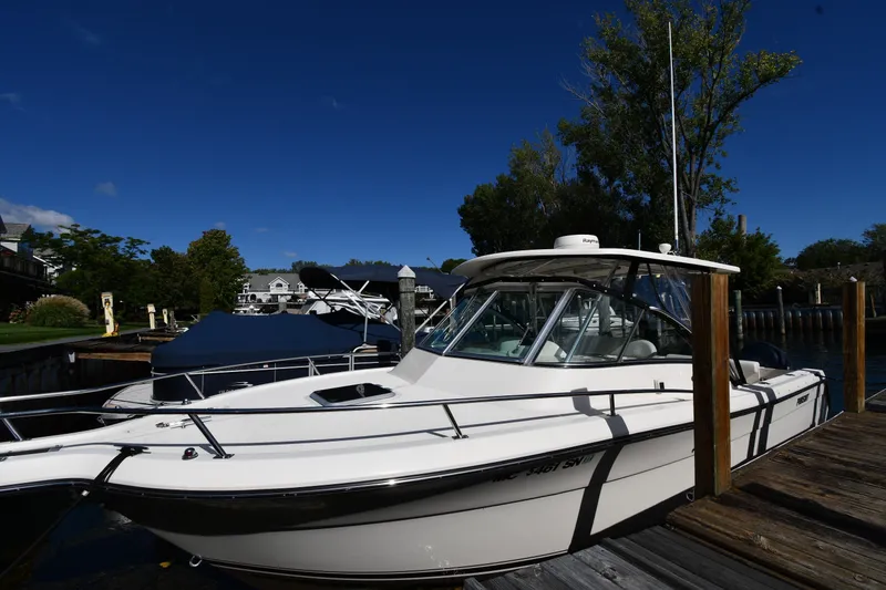 Slide: The Image of 2004 Pursuit 2670 Denali LS boat docked on a sunny day, surrounded by trees and buildings. - 1