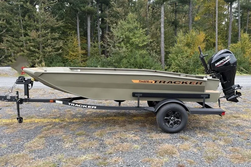 The Image of 2027 Tracker Grizzly 1553 Timber boat on trailer, parked outdoors with forest background. - 0