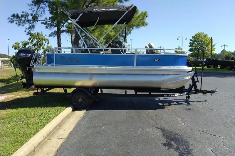 The Image of 2027 Sun Tracker Bass Buggy 18 DLX pontoon boat on trailer, parked outdoors. - 0