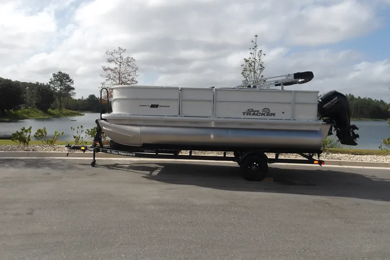 The Image of 2027 Sun Tracker Party Barge 18 DLX pontoon boat on trailer by a lake. - 0