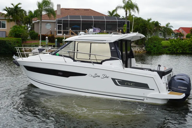 Slide: The Image of 2024 Jeanneau NC Sport 895 boat on a calm waterway, surrounded by lush greenery. - 2
