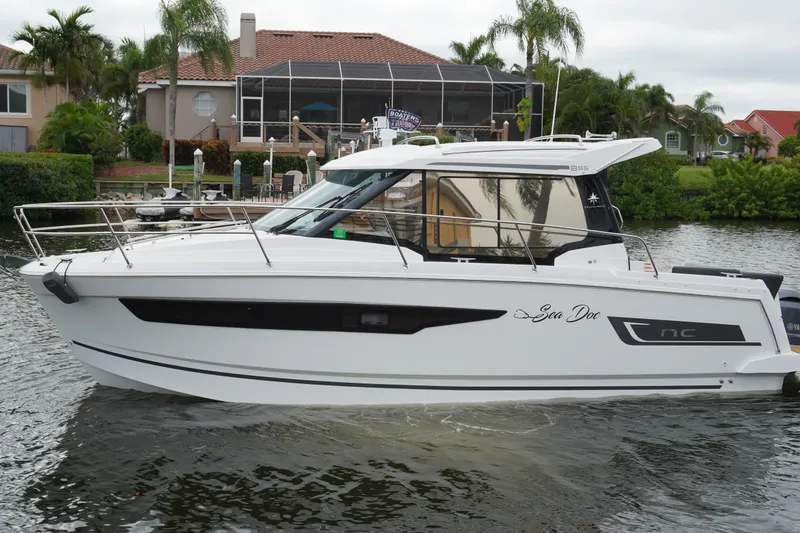 Slide: The Image of 2024 Jeanneau NC Sport 895 boat on water, surrounded by lush greenery and waterfront homes. - 1