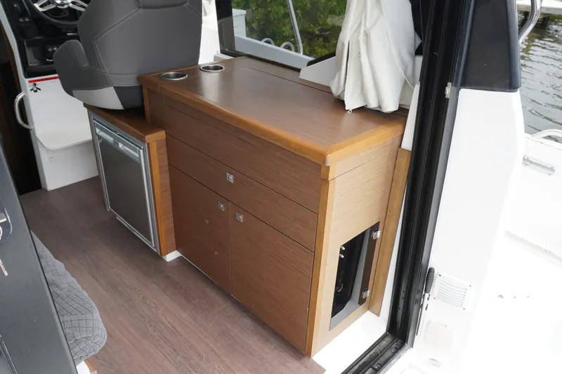 Slide: The Image of Interior view of 2024 Jeanneau NC Sport 895, featuring wooden cabinetry and compact fridge. - 14