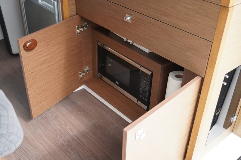 Slide: The Image of 2024 Jeanneau NC Sport 895 interior with built-in microwave and wooden cabinetry. - 15