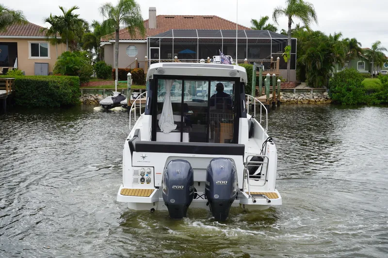Slide: The Image of 2024 Jeanneau NC Sport 895 boat with dual engines, navigating a residential canal. - 4