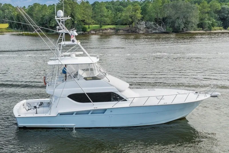 The Image of 2000 Hatteras 55 Convertible yacht cruising on a serene river with lush green surroundings. - 1