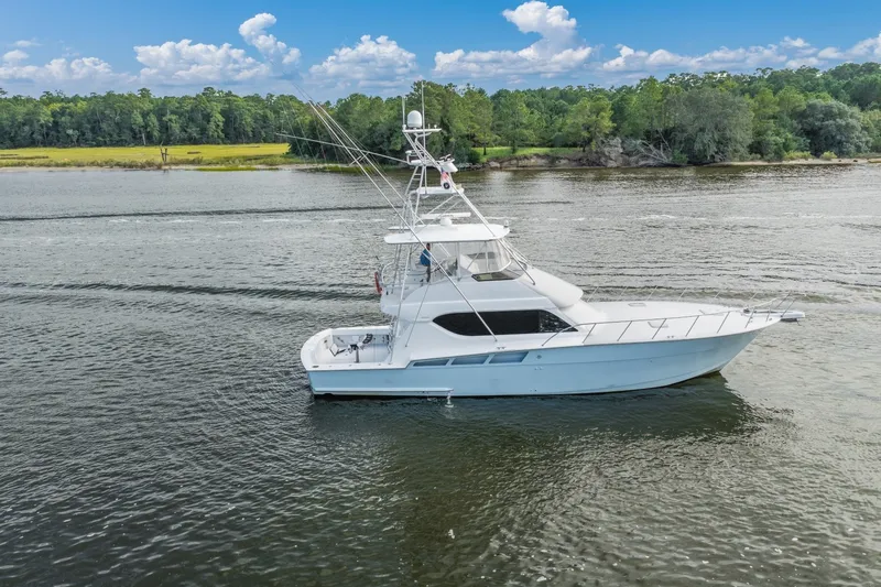 Slide: The Image of 2000 Hatteras 55 Convertible yacht cruising on a scenic river with lush green shoreline. - 2