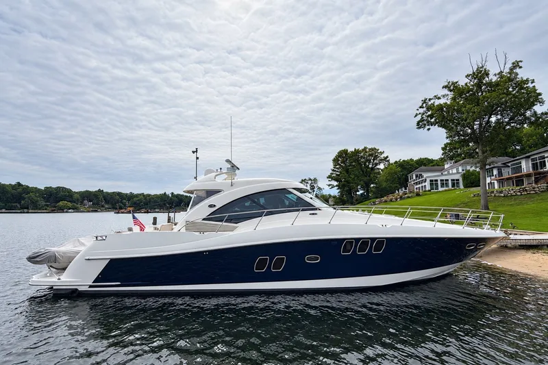 The Image of 2006 Sea Ray 60 Sundancer yacht docked by a scenic lakeside with houses. - 0
