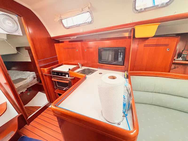 Slide: The Image of The interior of a 2005 Beneteau Oceanis Clipper 343 features a well-equipped galley with wood paneling, stove, sink, and microwave. - 27