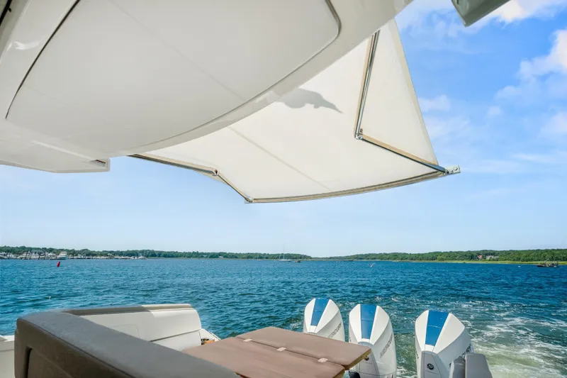 Slide: The Image of 2022 Tiara Yachts 38 LS with sunshade, overlooking serene blue waters and lush shoreline. - 23