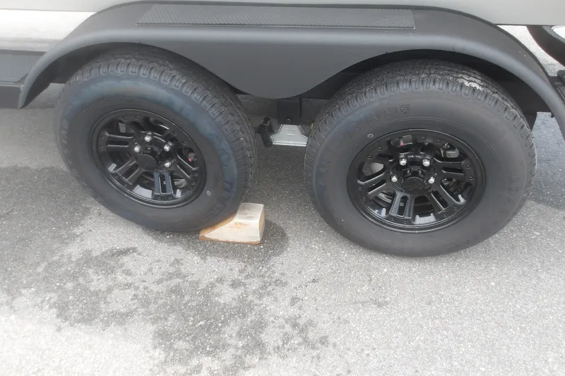 Slide: The Image of 2027 Ranger RT198P trailer wheels on pavement with black rims and wooden block. - 9