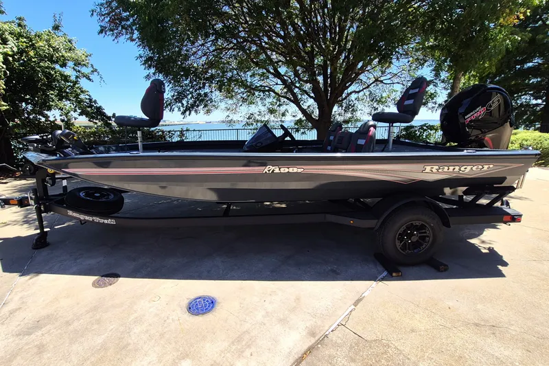The Image of 2027 Ranger RT198P fishing boat on trailer, parked outdoors under trees. - 0
