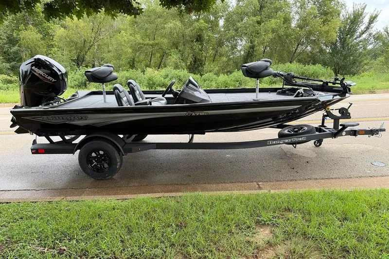 The Image of 2027 Ranger RT178C fishing boat on trailer, parked roadside with lush greenery background. - 0
