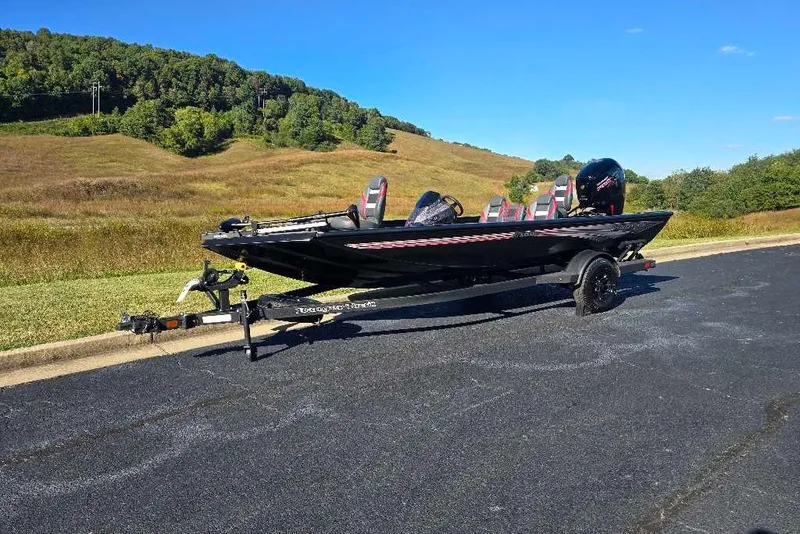 Slide: The Image of 2027 Ranger RT188C boat on trailer, parked on asphalt near grassy hills under clear blue sky. - 2