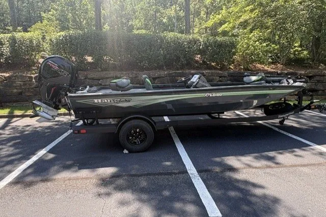 Slide: The Image of 2027 Ranger RT198P boat parked in a sunny lot, surrounded by greenery. - 2