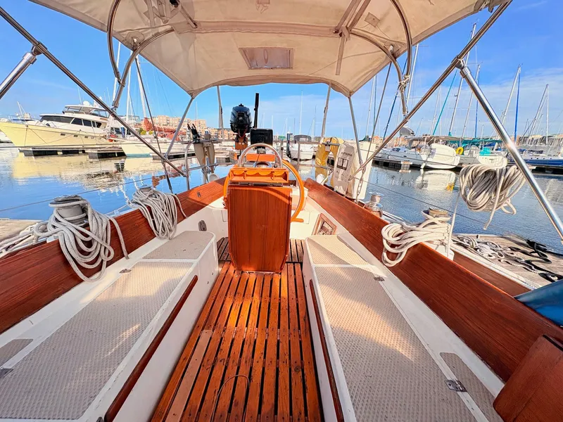 Slide: The Image of The cockpit of a 1979 Shannon 38 with wooden details and a steering wheel, docked in a marina. - 33