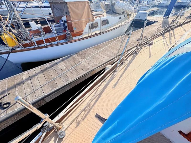 Slide: The Image of A sailboat docked at a wooden pier. It has a blue cover and is surrounded by other boats. - 34
