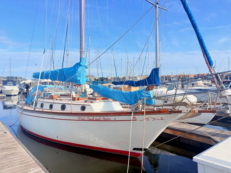 Slide: The Image of A 1979 white sailing yacht docked in a marina, featuring blue covers and wooden details. - 2