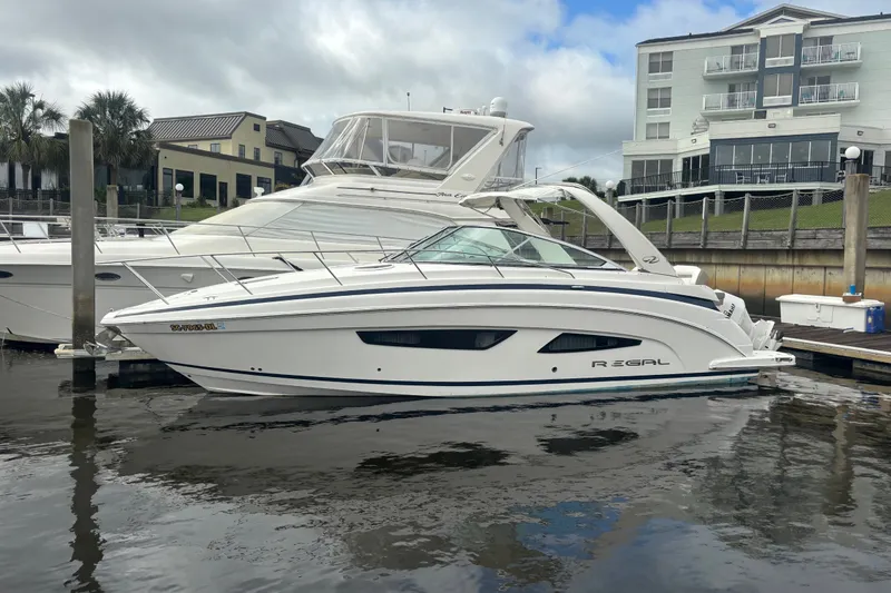 Slide: The Image of 2018 Regal 33 XO boat docked at marina, with modern buildings in background. - 2