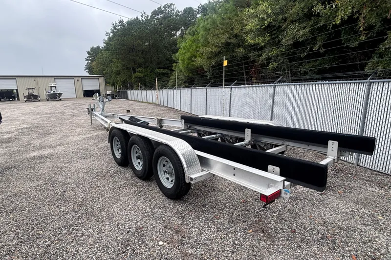 Slide: The Image of Triple-axle boat trailer parked on gravel near storage facility, surrounded by trees and fencing. - 41