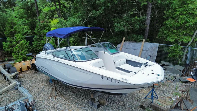 The Image of A white 2018 Regal 23 OBX boat is on a gravel lot, surrounded by trees. - 1