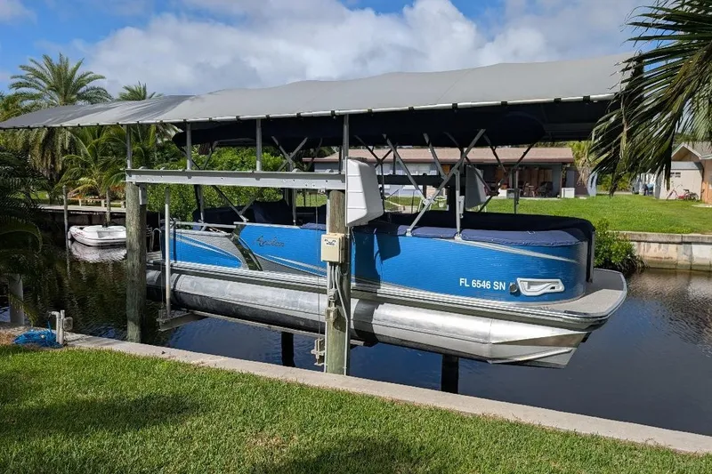 The Image of 2019 Avalon 2485LSZ pontoon boat docked under a canopy by a canal. - 0