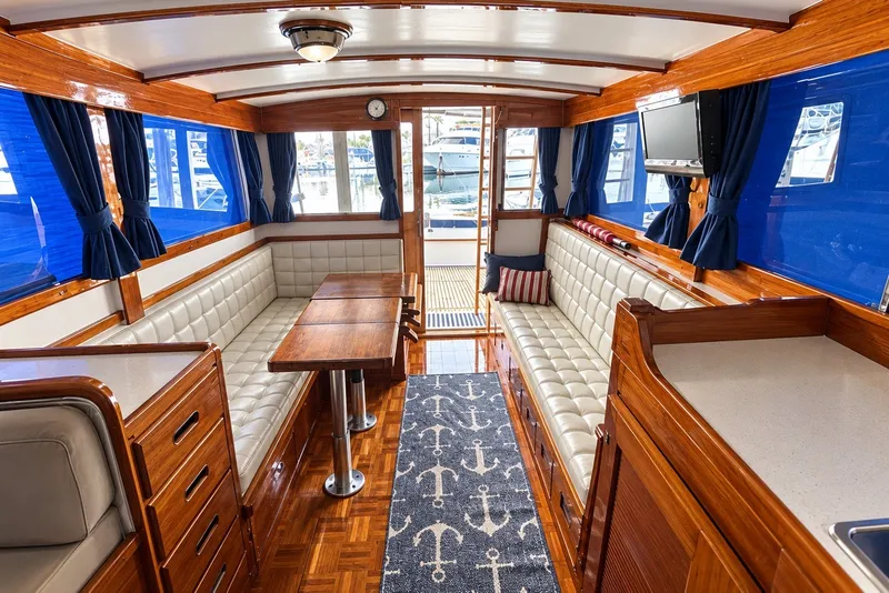 Slide: The Image of 1974 Grand Banks 32 Sedan interior with wood finish, blue curtains, and white seating. - 12